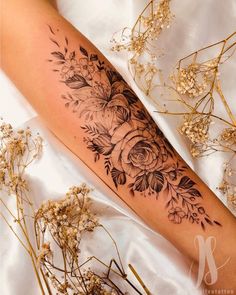 a woman's leg with flowers on it and some dried plants in the background