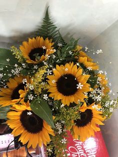 a bouquet of sunflowers and baby's breath in a red vase on a table