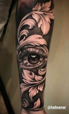 an eye tattoo on the arm with flowers and leaves around it, in black and white