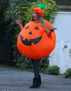 a woman in a pumpkin costume is walking down the street with an orange bag on her back