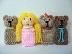 three knitted teddy bears are standing next to each other, one is wearing a pink dress and the other has a yellow wig