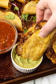 a person dipping guacamole into a bowl with salsa and tortilla bread