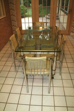 a glass dining table with four chairs in front of an open door and tiled floor