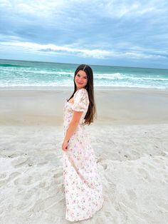 a woman standing on top of a sandy beach next to the ocean in a dress