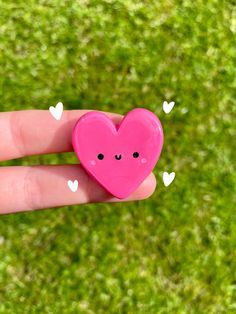 a small pink heart shaped object sitting on top of a persons hand in the grass