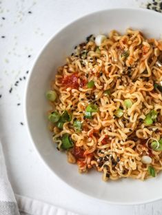 a bowl filled with noodles and vegetables on top of a white table cloth next to a spoon