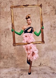 a woman in a dress and green gloves holding up a frame