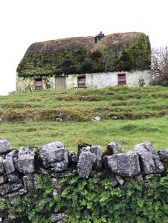 an old stone wall with moss growing on it and a building in the background that has two windows