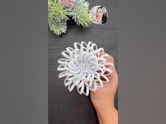 a hand holding a paper flower next to some succulents