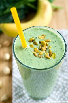 a green smoothie with nuts on top and a yellow straw in the cup next to it