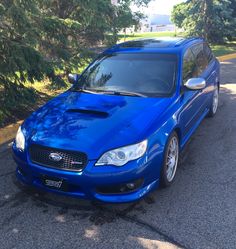 a blue subarunt is parked on the side of the road in front of some trees