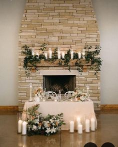 a table with candles and flowers on it in front of a fire place that is surrounded by greenery