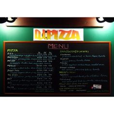 the menu for pizza is written on a blackboard in front of a green wall