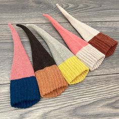 five different colors of knitted headbands laying on a wooden surface, one is multicolored