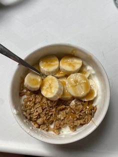 a bowl filled with granola and bananas on top of a white countertop next to a spoon