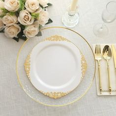 a table set with white and gold plates, silverware and flowers on the table