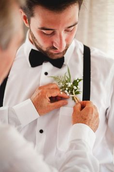 a man in a tuxedo adjusts the tie on another man's neck