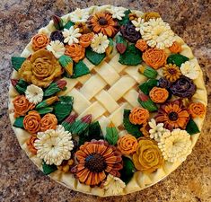 a pie decorated with flowers and leaves on a counter top in the shape of a flower arrangement