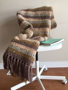 a blanket sitting on top of a white table next to a chair with a book