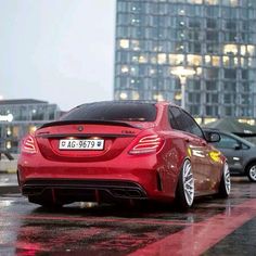 a red sports car parked in front of a tall building on a rainy day with its lights on