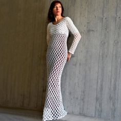 a woman wearing a white crochet dress standing in front of a concrete wall