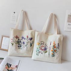 two bags with flowers painted on them sitting on a table next to an open book