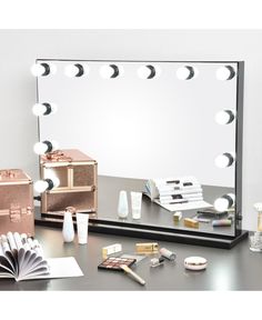 a vanity mirror with lights and cosmetics on it next to an open book, makeup case and other items