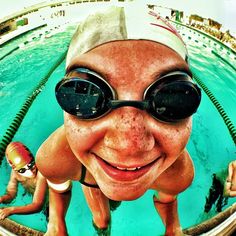 a man wearing goggles and swimming in a pool with other people on the side