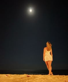 a woman is walking on the beach at night with her back turned to the camera