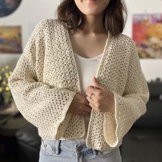 a woman standing in front of a couch wearing a white sweater and blue jeans with her hands on her hips