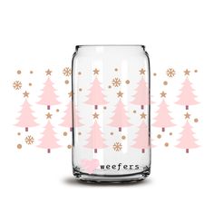 a glass jar filled with christmas trees on top of a white table next to pink and gold snowflakes