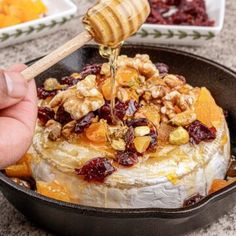 someone is pouring honey into a baked dessert in a pan with fruit and nuts on top