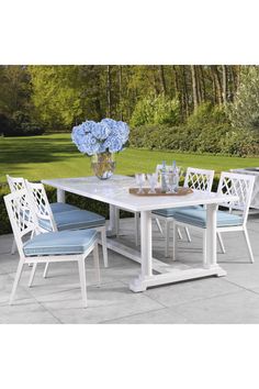 a white table with blue chairs and flowers in the vase on it's side