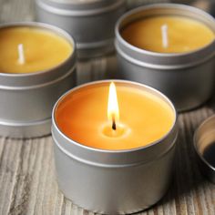 four beeswax candles sitting in tins on top of a wooden table with the words diy bourbon beeswax candles