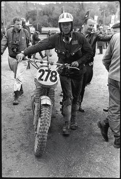 a man riding on the back of a motorcycle down a dirt road next to other people