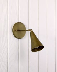 an antique brass wall light on a white painted wood paneled wall, with a cone shade