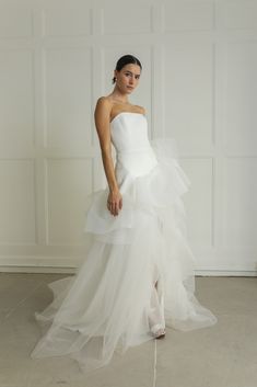 a woman in a white wedding dress standing on the floor with her hand on her hip