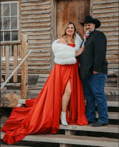 a man and woman standing next to each other in front of a wooden building wearing red dresses