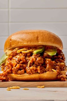 a pulled pork sandwich with pickles and cheese on a cutting board in front of a white brick wall