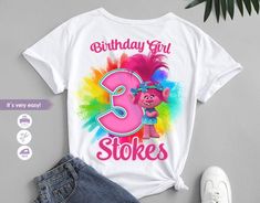 a birthday girl shirt with the number three in pink and blue on it, next to a pair of denim shorts