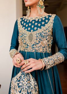 Blue Gold Long Pishwas for Pakistani Wedding Dresses are fully embroidered in the work of dabka, kora, tilla on sharara, and short shirt with net embellished dupatta. You are all set to make a lasting effect with this apparel. Long Pishwas: It is spun from rich teal Korean silk, and is a real embodiment of grace. It looks like something from a dream. This pishwas carried out as a remembrance of the splendor and grace of ageless beauty. It boasts a flawless tilla, an intricately embroidered bodic Pakistani Dress Design Wedding, Dress Design Wedding, Afghani Dresses, Classy Suits, Afghan Fashion, Girl Crush Fashion, Bridal Dress Fashion, Embroidered Bodice, Afghan Dresses