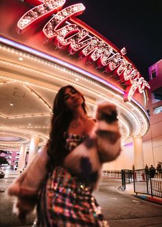 a woman standing in front of a building with lights on it's sides and her hand up to the sky