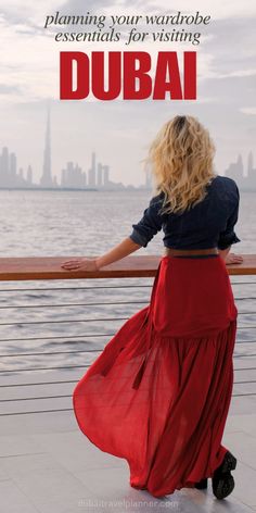 a woman in a red skirt is looking out over the water with her arms outstretched