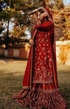 a woman in a red and gold bridal gown standing on grass with her arms around her head