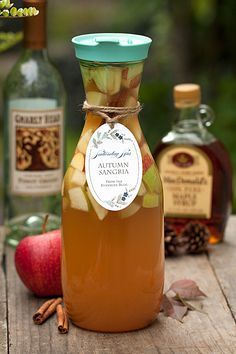 an apple cider with apples and cinnamons around it on a wooden table next to bottles