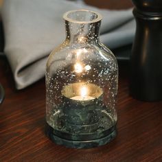 a glass jar with a candle inside on a table next to a pillow and other items