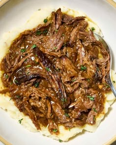 a white plate topped with mashed potatoes covered in beef and gravy next to a fork