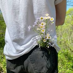 a person with their back to the camera, holding flowers in their jeans and wearing a white t - shirt