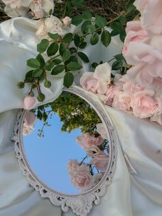 a mirror sitting on top of a white cloth covered ground next to pink flowers and greenery