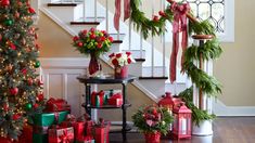 christmas decorations and presents are on display in front of the stairs with red bows, green garlands and lights